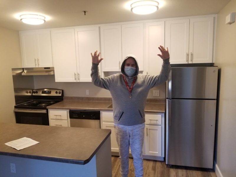 Picture of a male supported living services participant celebrating with hands up in the air in the kitchen of his new apartment.